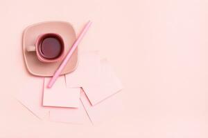 das Konzept ist Rosa. Rosa trinken im ein Kaffee Tasse, Schreiben Blätter und Stift auf ein Rosa Hintergrund. oben Sicht. Kopieren Raum foto
