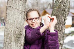 jung attraktiv Mädchen im Brille macht ein Herz gestalten mit Palmen im ein Stadt Park im früh Frühling foto