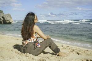 jung asiatisch Frau sitzen auf das Strand Sand. Porträt sexy asiatisch Dame Reisen und entspannend im das Sommer- mit tropisch Natur. foto