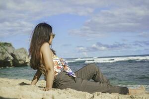 jung asiatisch Frau sitzen auf das Strand Sand. Porträt sexy asiatisch Dame Reisen und entspannend im das Sommer- mit tropisch Natur. foto