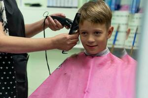 Haar Schneiden zum ein Kind mit ein Haar Clipper im ein Schönheit Salon foto