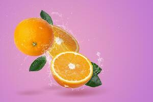 frisch geschnitten Orangen und Orange Obst und Wasser planschen auf ein Rosa Hintergrund. foto