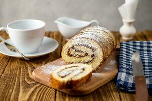 ungeschnitten Keks rollen mit Obst Marmelade und pulverisiert Zucker auf ein Schneiden Planke, mit ein Weiß Tee Tasse. hausgemacht Backen. Frühstück. foto