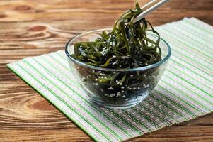 Seetang Salat. asiatisch Küche. Seetang Seetang im ein Glas Schüssel bestreut mit Sesam Samen, mit hölzern Stöcke. Laminaria foto