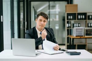 jung Geschäftsmann Arbeiten beim Büro mit Laptop, Tablette und nehmen Anmerkungen auf das Papier. foto