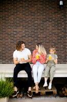 Familie mit ein Mutter, Vater und Tochter Sitzung draußen auf das Schritte von ein Vorderseite Veranda von ein Backstein Haus foto