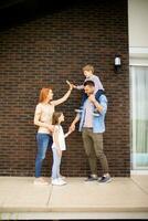 Familie mit ein Mutter, Vater, Sohn und Tochter Stehen durch das Mauer von Backstein Haus foto