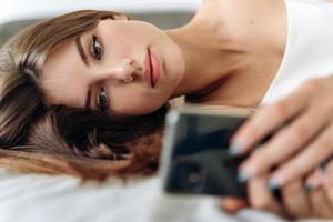 Frau schaut auf ihr Handy, während sie auf ihrem Bett liegt foto