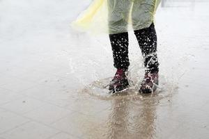 Frau, die im Regen spielt, mit Spritzern in Pfützen springt foto