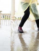 Frau, die im Regen spielt, mit Spritzern in Pfützen springt foto