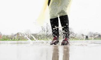 Frau, die im Regen spielt, mit Spritzern in Pfützen springt foto