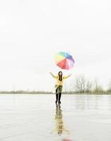 Lustige Frau, die draußen im Regen bunten Regenschirm fängt foto