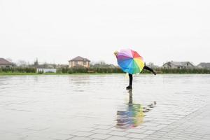 schöne brünette frau mit buntem regenschirm tanzt im regen