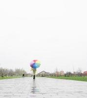 Frau mit buntem Regenschirm, die im Regen spazieren geht, Blick von hinten foto