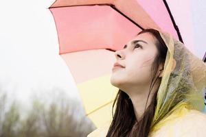 Frau, die einen regenbogenfarbenen Regenschirm hält und wegschaut foto