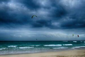 Sommer- Landschaft mit das Ozean mit dunkel wolkig Wellen und surfermi Kit mit Fallschirme schwebend auf das Ufer foto