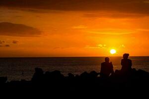 zwei Menschen Sitzung auf Felsen Aufpassen das Sonnenuntergang foto