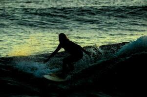 ein Surfer Fahrten ein Welle beim Sonnenuntergang foto