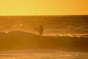 ein Mann Drachen Einsteigen im das Ozean beim Sonnenuntergang foto