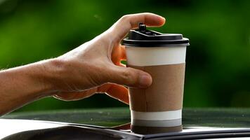 Kaffee wegbringen im ein Papier Tasse auf oben von das Auto Dach Grün Baum Hintergrund beim Sonnenaufgang im das Morgen, selektiv Fokus, Sanft Fokus. foto