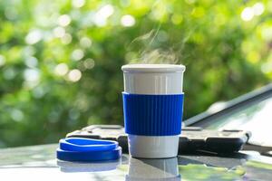 heiß Keramik Weiß Kaffee Tasse mit Rauch platziert draußen das Auto Instrumententafel beim Sonnenaufgang im das Morgen, im ein natürlich Hintergrund. heiß Kaffee trinken Konzept, selektiv Fokus, Sanft Fokus. foto