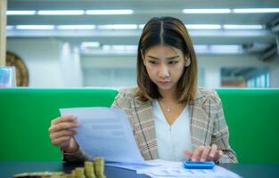 schön asiatisch Geschäft Frau ist Sitzung beim ein schwarz Tabelle suchen beim finanziell Unterlagen sie ist halten Papierkram im einer Hand und drücken auf ein Taschenrechner mit das andere Hand, Digital Marketing. foto