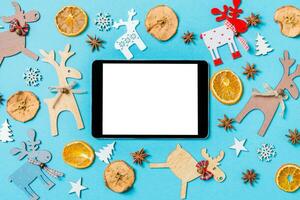 Draufsicht des digitalen Tablets auf blauem Hintergrund aus Weihnachtsdekorationen und Spielzeug. Weihnachtsschmuck-Konzept foto