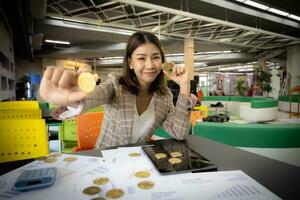 schön asiatisch Geschäftsfrau ist gezeigt halten ein Bitcoin im ihr Hand mit ein dokumentieren sichtbar auf ihr Schreibtisch. foto