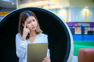 schön asiatisch Geschäft Frau ist Sitzung auf ein modern runden Stuhl halten ein Tablette mit ein Befragung sehen, Digital Marketing. foto