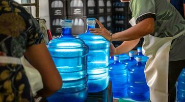 Arbeitskräfte Aufzug Gallonen von Blau Trinken Wasser und Flaschen im Kisten in das zurück von ein Transport LKW. foto