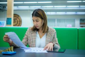 jung schön asiatisch Geschäft Frau ist Sitzung und suchen beim finanziell Unterlagen, mit einer Hand berühren ein Tablette, Digital Marketing. foto