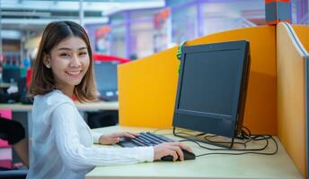 schön asiatisch Geschäft Frau ist Sitzung und mit ein Computer während gegenüber das Kamera mit ein lächeln, Digital Marketing. foto