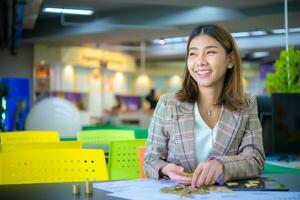glücklich schön asiatisch Geschäft Frau halten ein Stapel von Gold Münzen platziert auf ein schwarz Tabelle während suchen zu das Kopieren Raum mit Lächeln auf ihr Gesicht. foto