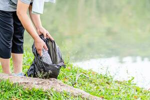 Eine Frau räumt auf, indem sie Plastikflaschen an einem natürlichen Wasserreservoir aufhebt. konzept zum schutz der umwelt, zur rettung der welt, zum recycling, zur reduzierung der globalen erwärmung. Nahaufnahme, unscharfer Hintergrund foto