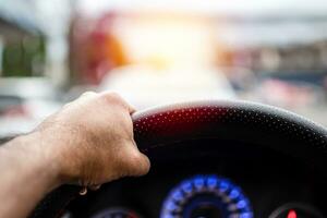 ein Mann Fahren ein links Hand zu halt das Lenkung Rad zu Steuerung das Auto vorsichtig während der Verkehr Stau, hat Copyspace auf oben zum Eingang Text, nehmen ein Nahansicht Schuss, verschwommen Hintergrund foto