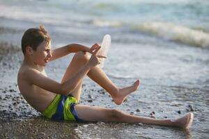 ein Teenager Junge ist Sitzung auf das Strand. foto