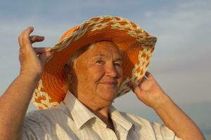 schön Alten Frau im ein Hut auf das Hintergrund von das Meer. Gesicht von ein alt Frau mit ein lächeln. foto