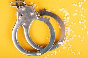 Handschellen und Kristalldrogen auf gelbem Hintergrund, Verhaftung eines Drogendealers. foto