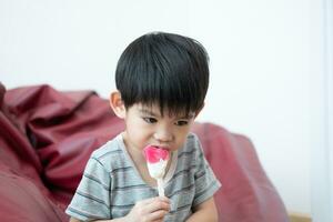 ein asiatisch Junge ist Essen köstlich Eis Sahne im ein Stuhl. foto