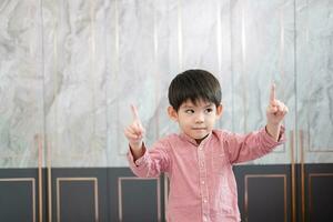 ein asiatisch Junge steht und lächelt, erziehen beide Hände und zeigen nach oben. foto