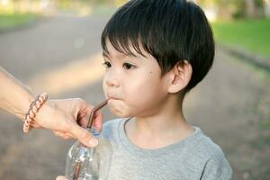 asiatisch Junge Trinken Wasser von ein Flasche gehaltenen durch seine Mutter foto
