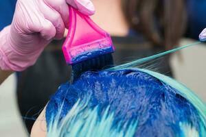 Friseur bewirbt sich Blau Farbe zu weiblich mit Smaragd Haar Farbe während Prozess von Färberei Haar im einzigartig Farbe foto