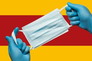 Medizin halten Atemwege Gesicht Maske im Hände im Blau Handschuhe auf Hintergrund Flagge von Spanien. Konzept Coronavirus Quarantäne, Pandemie Ausbruch foto