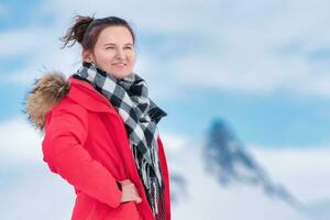 Porträt von Frau Reisender gekleidet im rot Winter Jacke, Schal auf Hintergrund von Berge, Blau Himmel mit Wolken foto