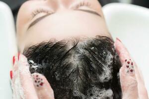 Friseur waschen lange Haar von Brünette Frau mit Shampoo im sinken zum Haarwäsche foto