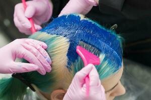 zwei Friseure mit Rosa Bürste während bewirbt sich Blau Farbe zu Kunde während Prozess von Färberei ihr Haar im einzigartig Farbe foto