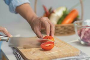 Kochen - - Koch Hände sind Schneiden Tomaten auf das Hacken Tafel im das Küche. vorbereiten Schweinefleisch Lager mit Gemüse Brühe im ein Topf. hausgemacht Bouillon Rezept. foto