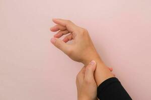 Nahansicht von Frau Hand halten ihr schmerzlich Handgelenk von Arthritis oder Karpal Tunnel Syndrom cst isoliert auf Rosa Hintergrund. Gesundheit Pflege Konzept. foto