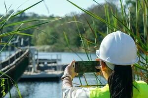 Umwelt Ingenieur Verwendet ein Handy, Mobiltelefon Telefon zu nehmen Bilder und Aufzeichnung Daten Analysieren Sauerstoff Ebenen im das Reservoir. Wasser und Ökologie Konzept. foto