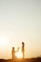 Silhouette eines Mannes, der bei Sonnenuntergang mit seiner Freundin zur Heirat kniet
